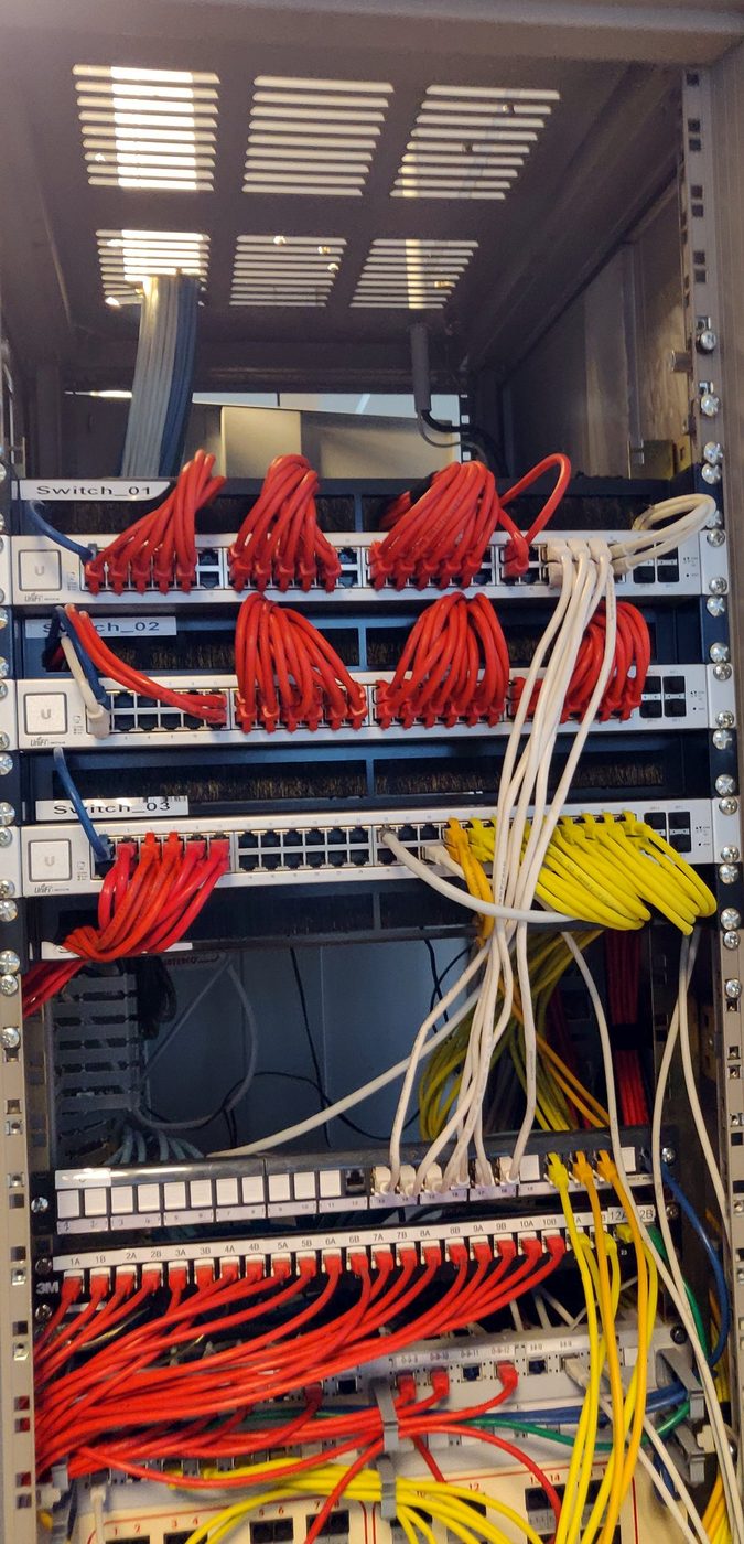 Panneaux de brassage réseau, cordons rouges et jaunes soigneusement peignés.
